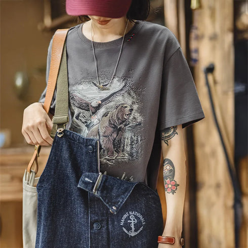 Person wearing a graphic t-shirt with an owl design, denim overalls, and a pink hat.